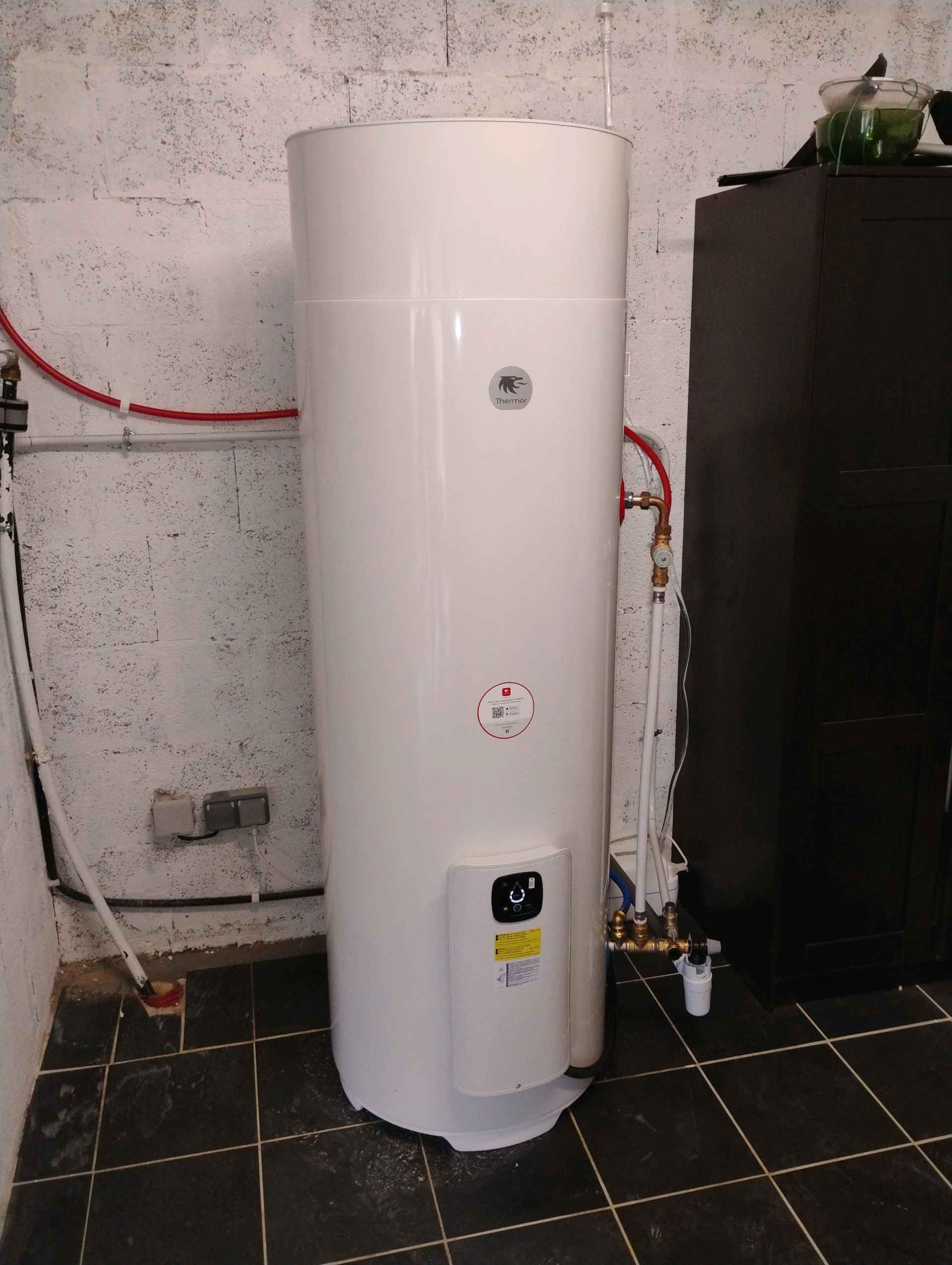 Chauffe-eau thermodynamique Thermor : installation et guide Chauffe-eau thermodynamique blanc Thermor installé avec tuyauterie apparente dans une buanderie.