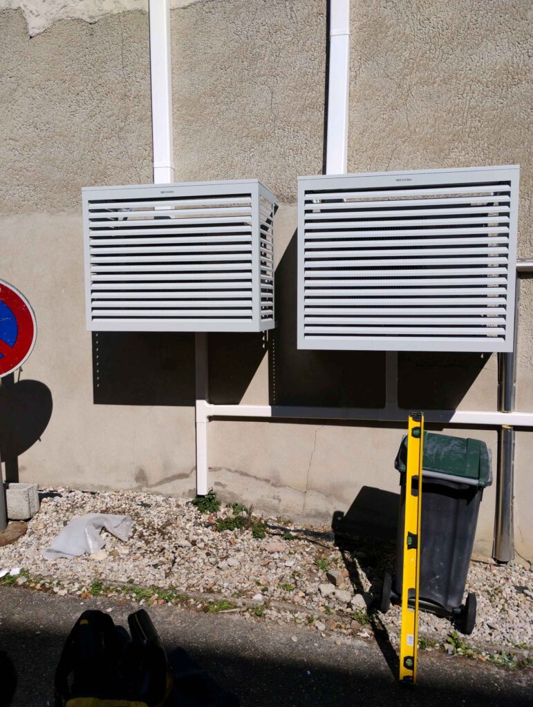 Deux unités de climatisation extérieure avec caches Decoclim blancs installés sur un mur de façade avec goulottes.