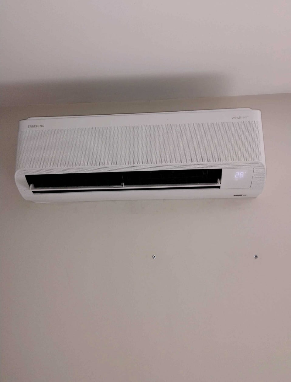 Climatiseur mural Samsung WindFree blanc affichant 28 degrés, installé sur un mur intérieur clair.