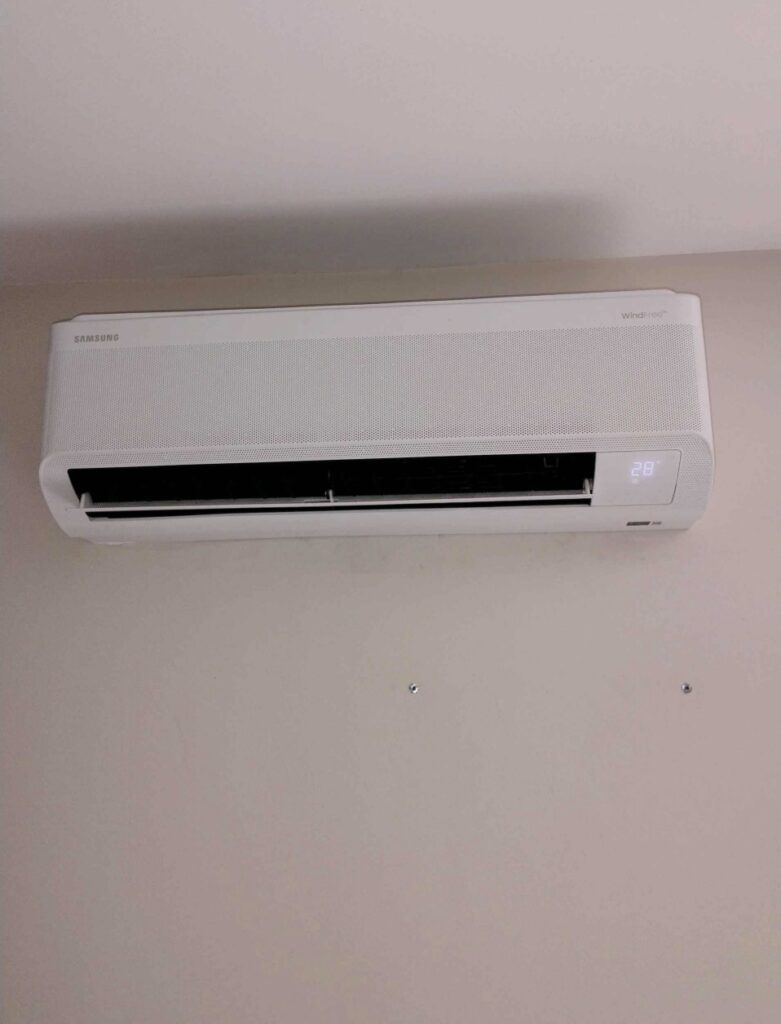 Climatiseur Samsung WindFree : Confort et Design Mural Climatiseur mural blanc Samsung WindFree avec affichage numérique à 28 degrés sur un mur clair.