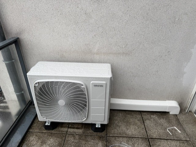 Installation Climatiseur Atlantic : Unité de Balcon Unité extérieure de climatiseur Atlantic installée sur un balcon carrelé avec goulotte de protection blanche.
