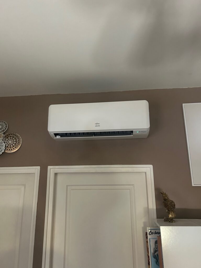 Climatiseur Fujitsu Atlantic blanc installé sur un mur brun au-dessus d'une porte blanche.