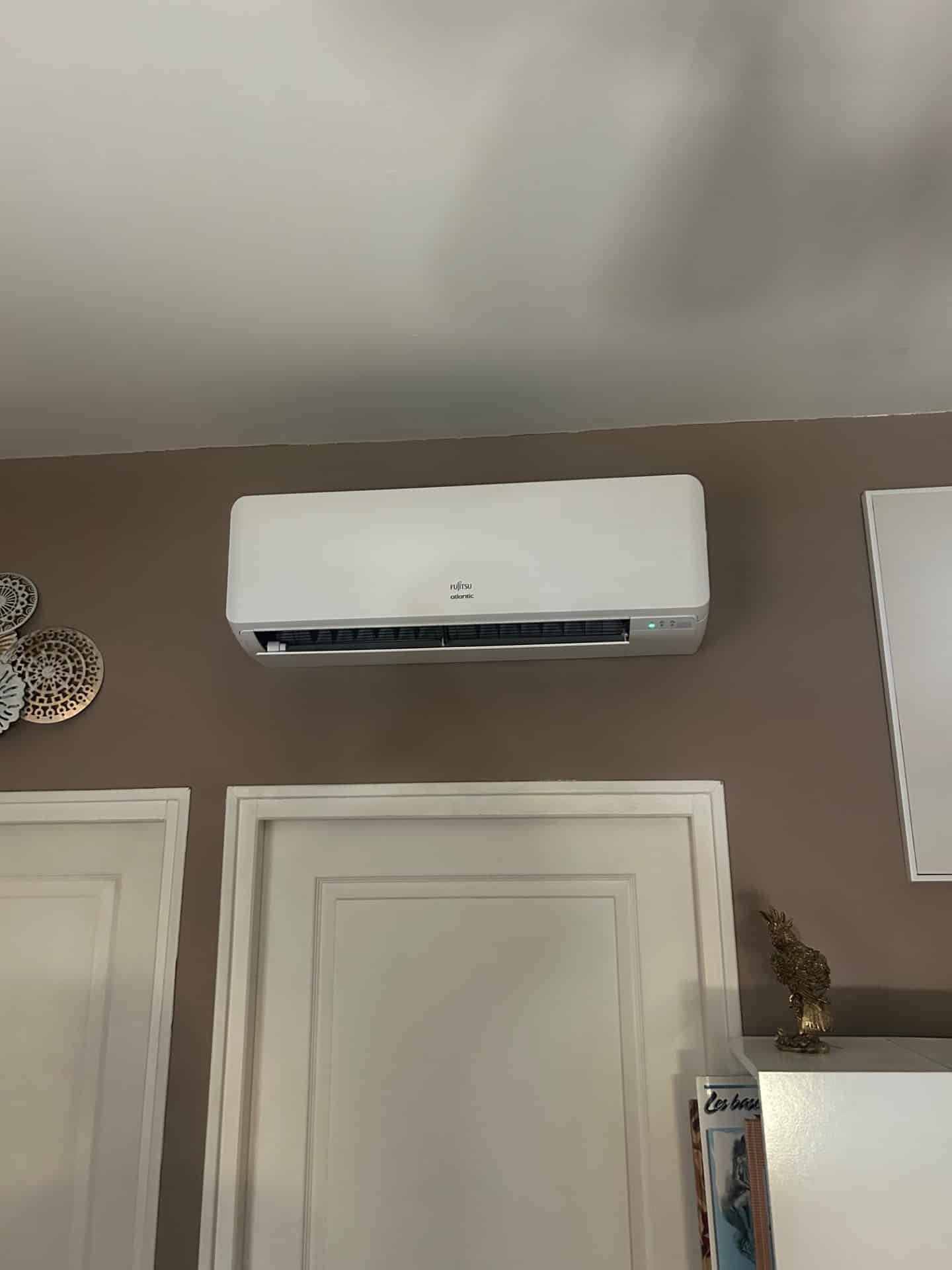 Climatiseur Fujitsu Atlantic : Installation murale élégante Climatiseur Fujitsu Atlantic blanc installé sur un mur brun au-dessus d'une porte blanche.