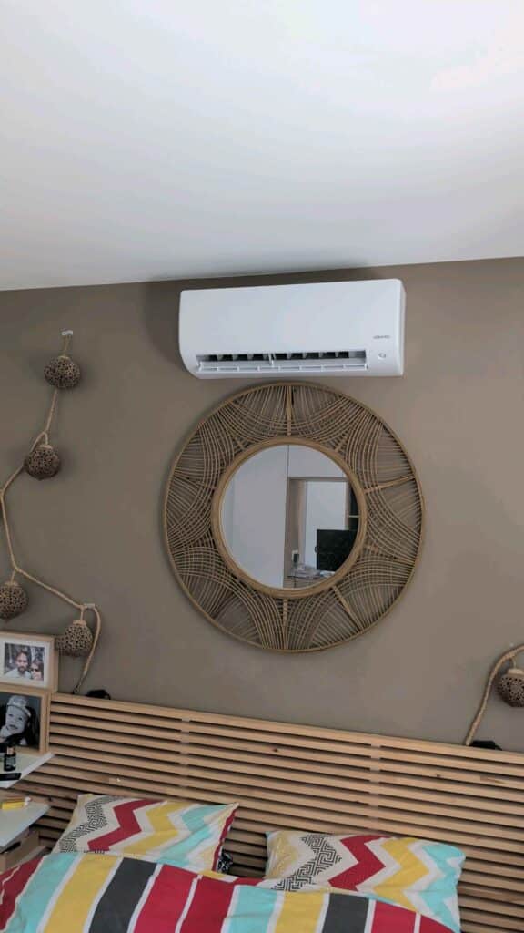 Climatiseur Atlantic blanc et miroir soleil en rotin décorant une chambre au mur taupe.