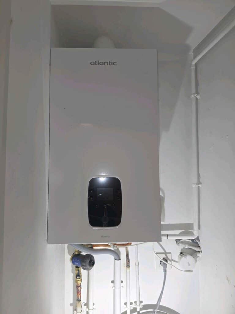Chaudière gaz murale Atlantic Naema blanche avec écran digital et tuyauterie apparente.